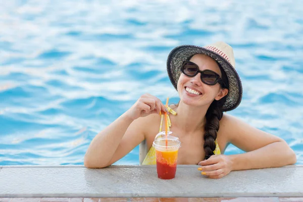 Gülümseyen kadın yüzme havuzunda meyve suyu içiyor.