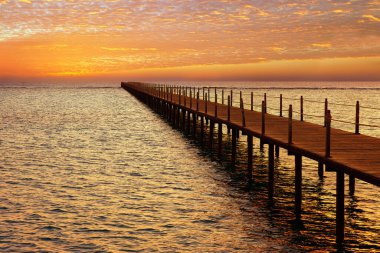 wooden pontoon bridge in sea and picturesque sky with spindrift clouds on sunrise