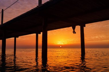 Gün doğumunda güzel deniz manzaralı ahşap köprüde oturan kadın bacakları