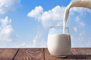 Süt sürahide bardağa doluyor mavi gökyüzü ve arka planda bulutlar