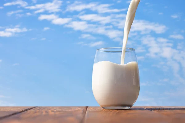 Leche Vertiendo Vaso Sobre Mesa Con Cielo Azul Las Nubes — Foto de Stock