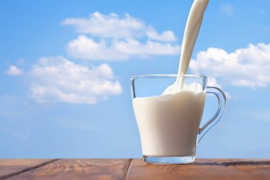 Süt cam bardağa doluyor mavi gökyüzü ve arka planda bulutlar