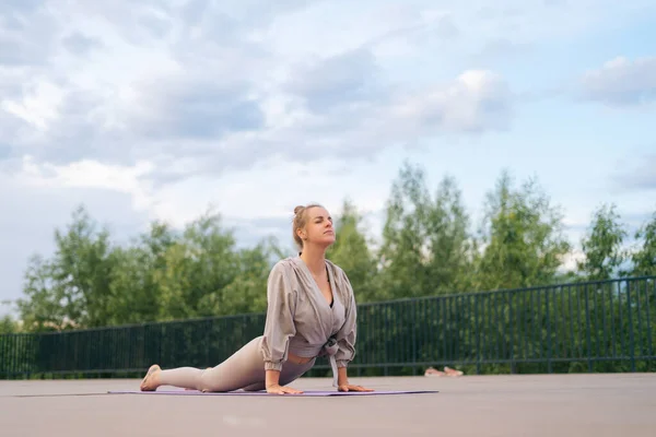 Flexible young woman with sporty body doing yoga exercise Upward Wheel or Bow Pose lying on yoga mat in city park. Y