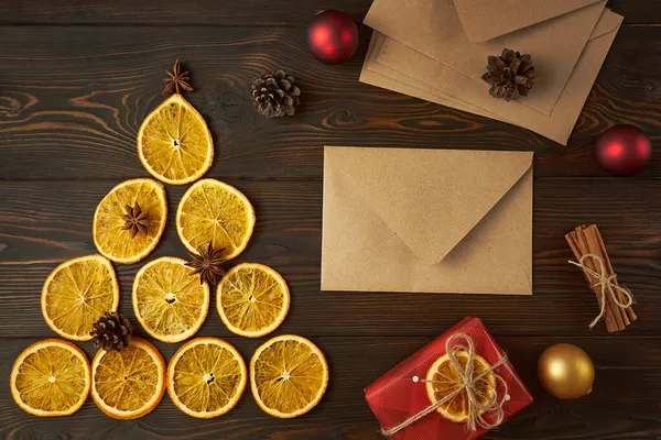 Kuru portakallardan yapılmış Noel ağacı ve koyu kahverengi ahşap bir zemin üzerindeki zarflar. Yaratıcı festival dekorasyon konsepti.