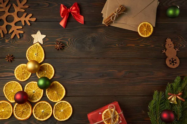 Kuru portakallardan yapılmış Noel ağacı ve koyu kahverengi ahşap bir zemin üzerindeki zarflar. Yaratıcı festival dekorasyon konsepti.