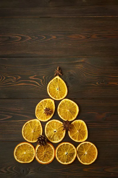 Kuru portakaldan yapılmış Noel ağacı, koyu kahverengi ahşap arka planda yıldız anason ve koni. Yaratıcı festival konsepti.