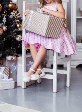 Pembe elbiseli küçük kız bir sandalyeye oturur ve yeni yıl hediyesini açar. Fotoğraf.