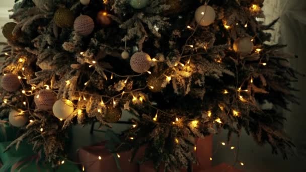 Ein schöner Weihnachtsbaum, geschmückt mit weißen und blauen Kugeln und einem leuchtenden Kranz. Die Kamera bewegt sich von unten nach oben. — Stockvideo