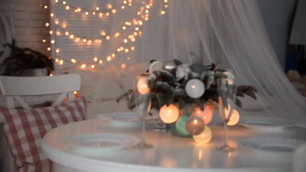 Πρωτοχρονιάτικη διακόσμηση στο τραπέζι. Το τραπέζι είναι διακοσμημένο με ένα βάζο με κλαδιά χριστουγεννιάτικου δέντρου και μια γιρλάντα από λαμπερές μπάλες. — Αρχείο Βίντεο