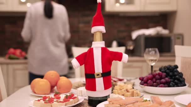 Kadın arkadaşlar bir araya gelir ve Noel veya Yeni Yıl yemeği hazırlar, sofrayı kurar, bulaşıkları yıkarlar. Noel Baba kostümündeki bir şişe şaraba odaklan.. — Stok video