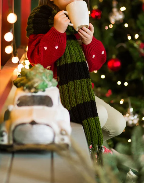 Child Cup Hot Drink His Hands Sits Background Christmas Tree — Stock Photo, Image