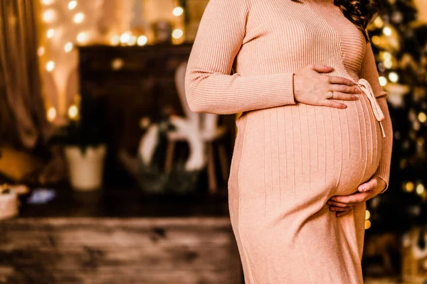 怀孕的女人抱着她的肚子 在圣诞节装饰的背景下摆姿势 — 图库照片