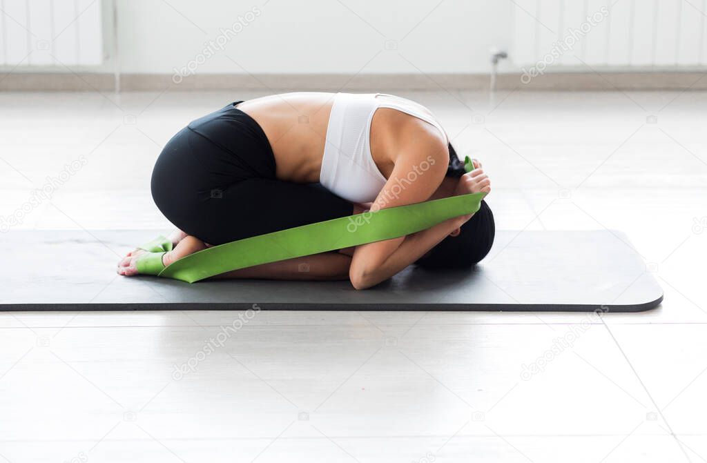 A girl in a white top and black cycling shorts posing in a fetal position pulling on a gymnastic ribbon. Horizontal photo