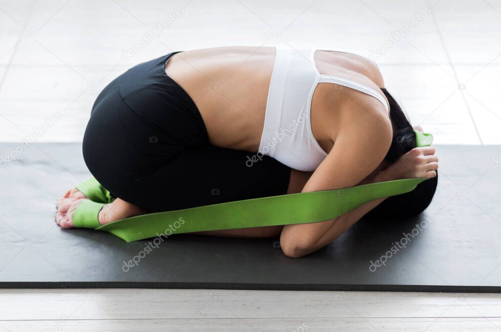 A girl in a white top and black cycling shorts posing in a fetal position pulling on a gymnastic ribbon. Horizontal photo