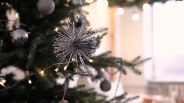 クリスマスツリーには サーバーカラーと丸みを帯びた形のクリスマスツリーのおもちゃが掛けられています 背景はガーランドで装飾されたベッドです — ストック動画