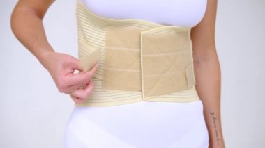 woman wearing beige support belt isolated on white. The girl fastens the belt