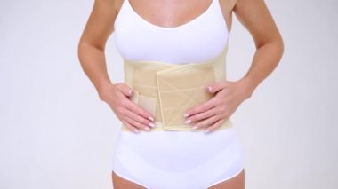 woman wearing beige support belt isolated on white. The girl demonstrates the belt to the camera and touches it with her hands