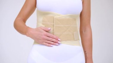 woman wearing beige support belt isolated on white. The girl demonstrates the belt to the camera and touches it with her hands