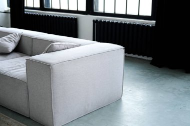 Modern bir evde rahat bir kanepenin yüksek açılı görüntüsü. Oturma odasındaki gri bir koltuğun yatay görüntüsü ve daire tasarımı. Oturma odasındaki beton zeminde metal parmaklıklar ve halı olan büyük bir pencere.