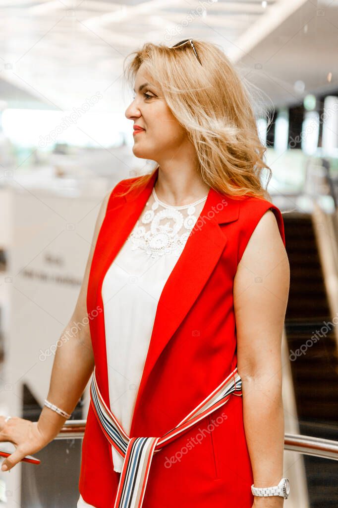 Beautiful mature woman in a white and red suit posing in the elevator of a shopping center. Woman planning to make purchases