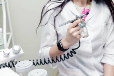 Güzellik uzmanı elinde oksijen enjeksiyonu tabancasıyla güzellik makinesinin yanında poz veriyor. Yatay fotoğraf