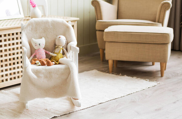 Handmade toys kitten and rabbit sit in a chair in the living room. Photo