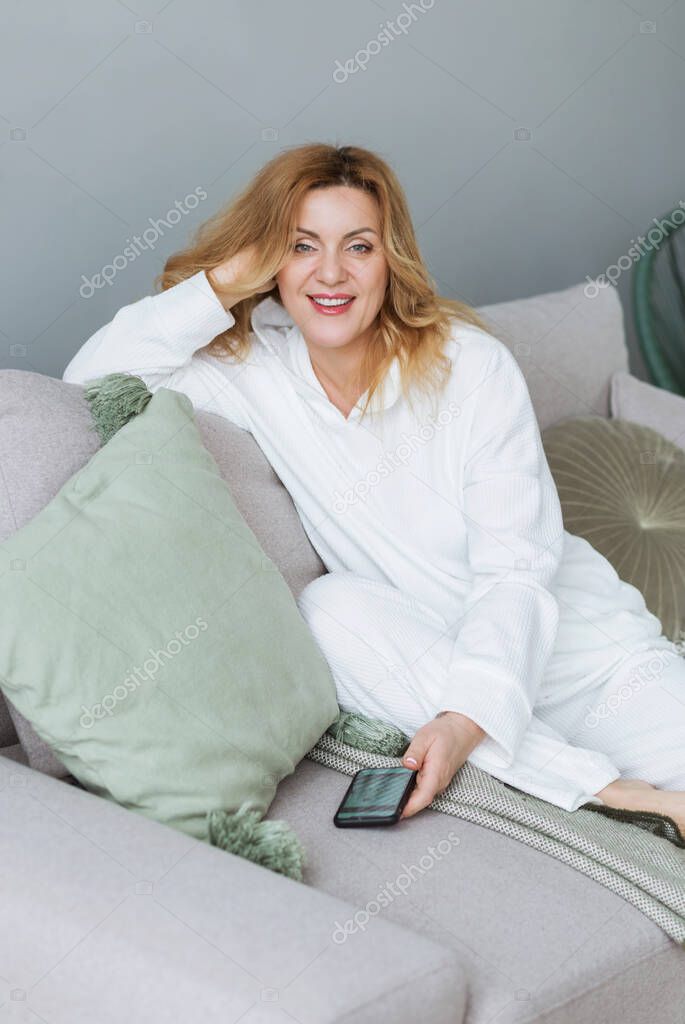 Lovely middle-aged blond woman with a beaming smile sitting on a sofa at home looking at the camera. Photo