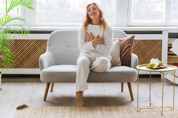 Woman White Clothes Reads Couch Home Hugs Piece Paper Her — Stock Photo, Image