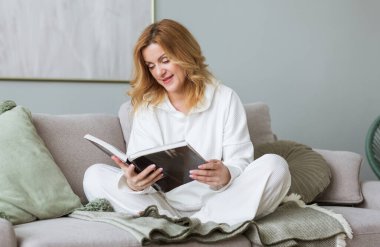 Kanepede oturan ve kitap okuyan bir kadın. Sosyal medya detoksu. Yavaş yaşam tarzı. Karantinada zihinsel refah. Edebiyattan hoşlanan mutlu kadın. Sakin kitap kurdu, bütün günü aletlerle geçiriyor.