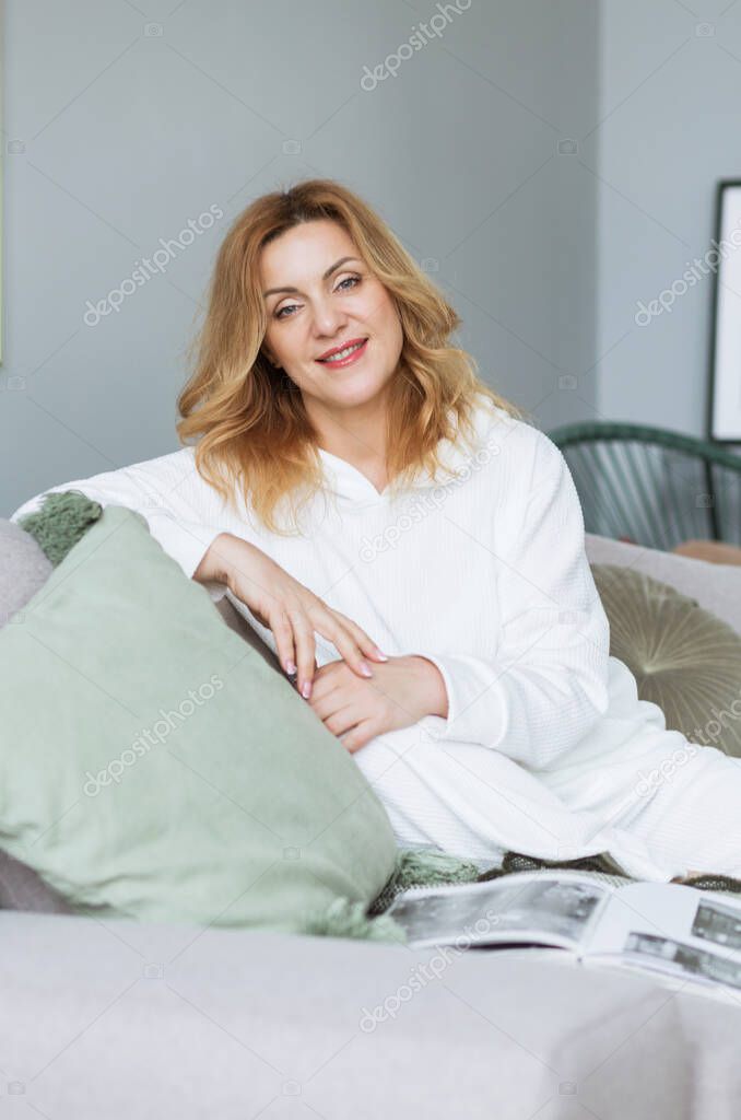 Lovely middle-aged blond woman with a beaming smile sitting on a sofa at home looking at the camera. Photo