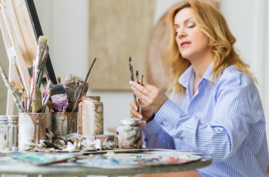 Evde tuvale fırça süren olgun bir kadın..