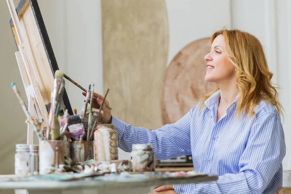 Stüdyoda tuvale fırça süren olgun bir kadın..