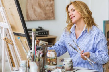 Evde tuvale fırça süren olgun bir kadın..