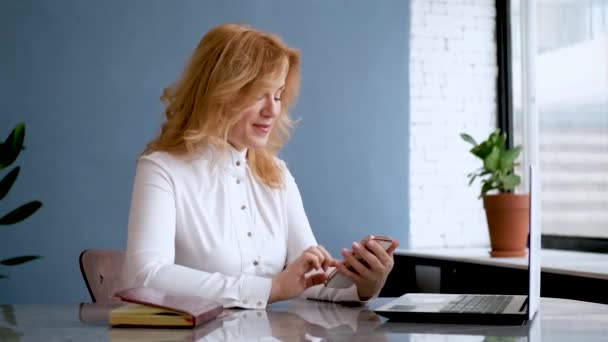Mulher bonita empresária senta-se no escritório e usa um telefone móvel — Vídeo de Stock