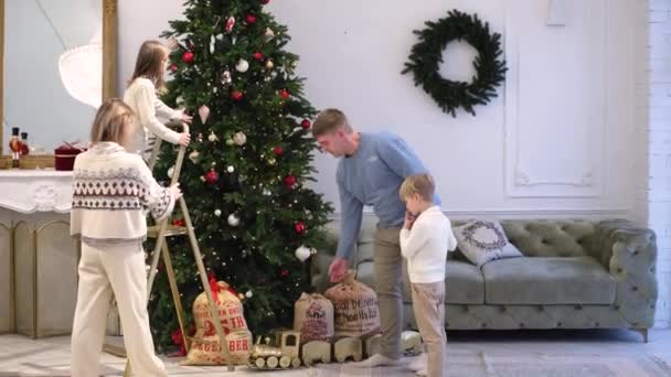 A family of four decorates the Christmas tree together — Stock Video