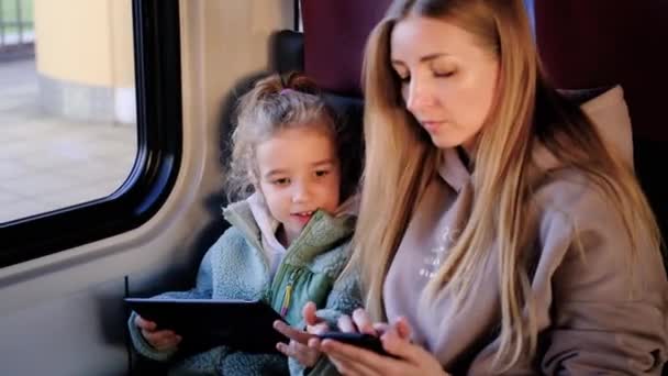 母親と娘は窓の近くの電車の中で座って話をしている彼らの手にガジェットを保持. — ストック動画