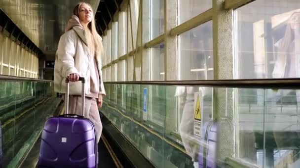 Donna nella passerella in movimento all'aeroporto con una valigia viola. — Video Stock