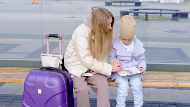 Mom helps her daughter draw while they are sitting at the bus stop waiting for the bus — Stock Video