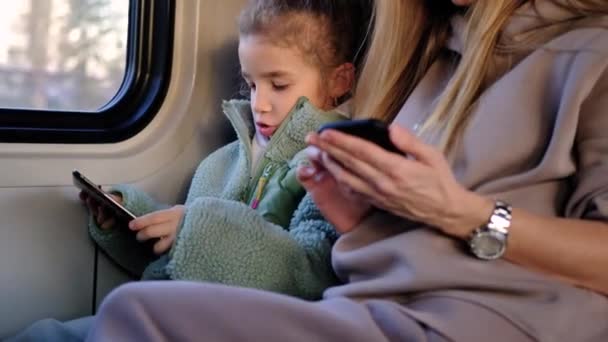 Mor og datter sitter på toget og leker i telefonen. – stockvideo