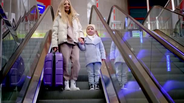 Madre e hija bajan por la escalera mecánica en el edificio del aeropuerto — Vídeos de Stock