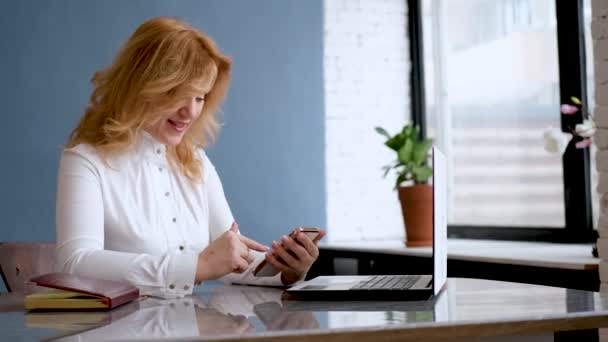 Mooie vrouw ondernemer zit in het kantoor en maakt gebruik van een mobiele telefoon — Stockvideo