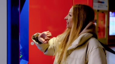 Ceketli genç bir kadın tren ya da metro bileti alıyor. 