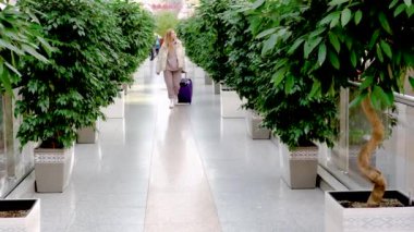  Havaalanında bavulları olan güzel bir kadın yeşil bitkilerle bekleme salonunda bekliyor.