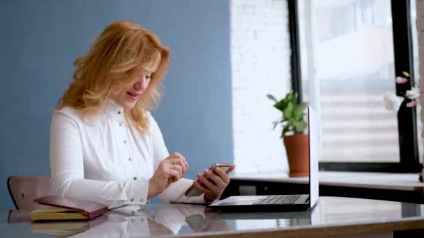 Mujer hermosa empresaria se sienta en la oficina y utiliza un teléfono móvil — Vídeos de Stock