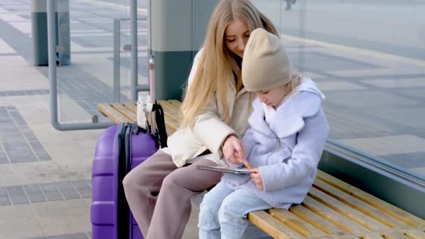 Máma pomáhá její dceři kreslit, zatímco oni sedí na autobusové zastávce čeká na autobus — Stock video