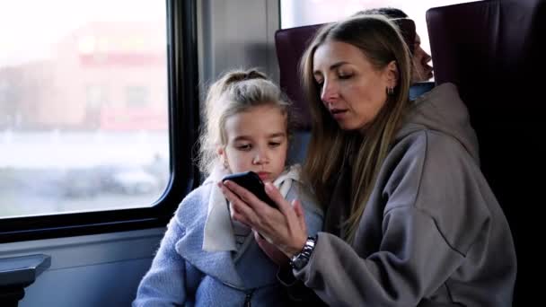 Mom and daughter ride the train and play a game on the phone — Stock Video