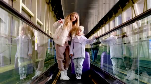 Mor og datter går ned rulletrappen fra stasjonsbygningen til plattformen – stockvideo