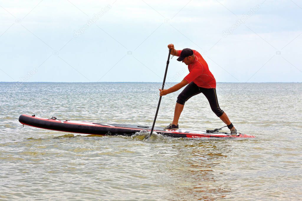Joyful man is training on a SUP board on a sea. Stand up paddle boarding