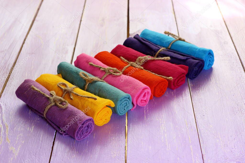 Rolls of multicolored clothes bound by a piece of rope stacked in a row on purple boards background