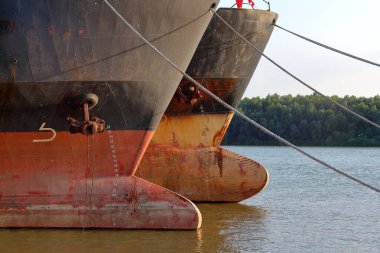 Prows of two old rusty ships with anchor chain anchored at Danube river at summer clipart